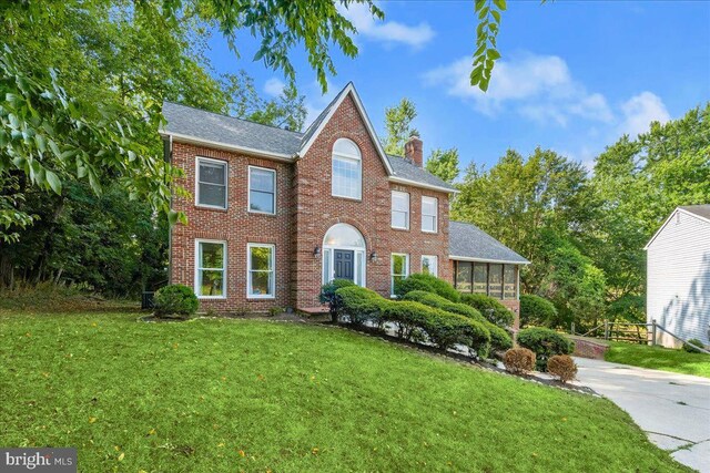 17 Alexandria Overlook Dr, Oxon Hill, MD 20745 - colonial inspired home featuring a front yard, roof with shingles, a sunroom, a chimney, and brick siding