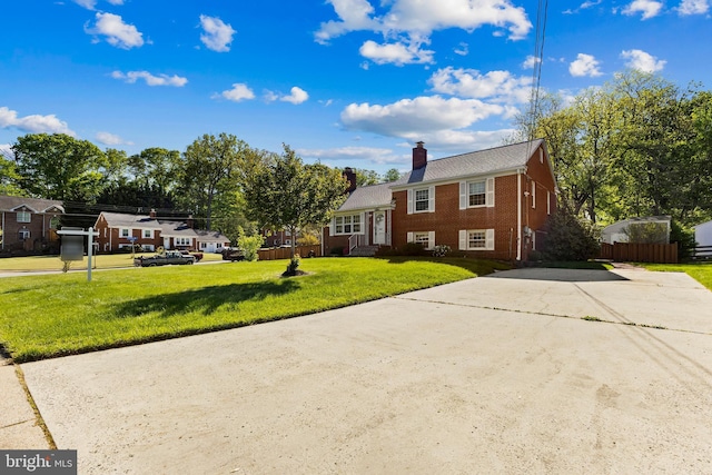 view of front of house featuring fence, a front yard, a chimney, brick siding, and concrete driveway