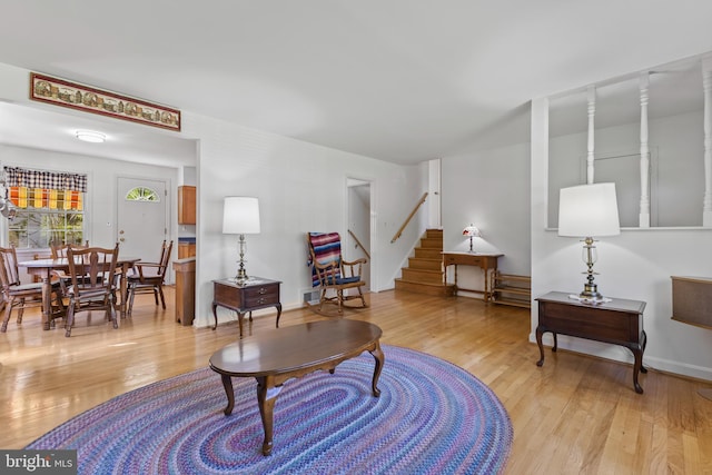 living room featuring baseboards, light wood finished floors, and stairs