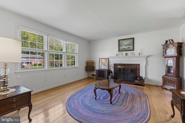 living room with baseboards, a brick fireplace, and wood finished floors