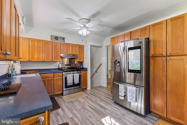 kitchen featuring brown cabinets, ceiling fan, appliances with stainless steel finishes, dark countertops, and a sink