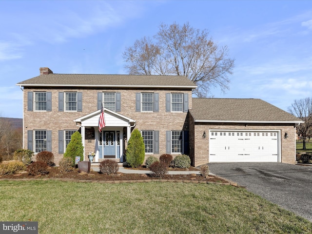 colonial-style house with aphalt driveway, an attached garage, a chimney, and brick siding