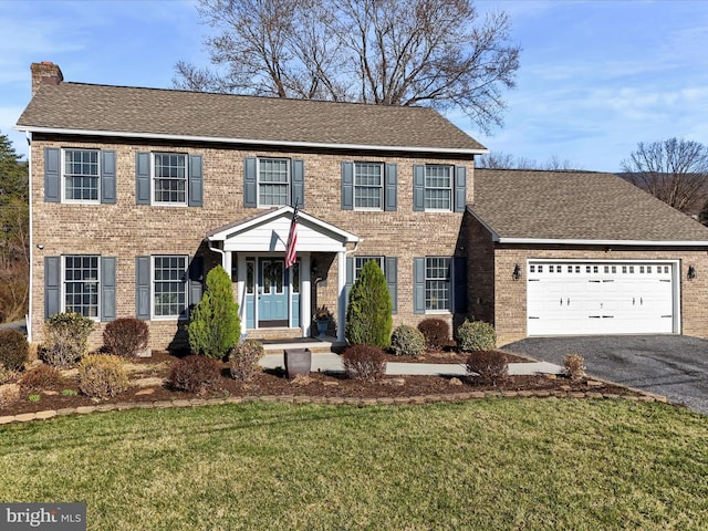 colonial home with a garage, a front yard, brick siding, and driveway