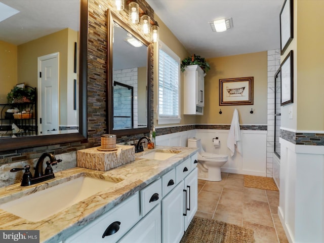 full bath with tile patterned floors, toilet, wainscoting, and a sink