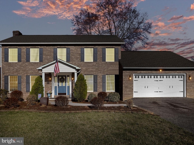 colonial house featuring aphalt driveway, brick siding, an attached garage, and a lawn
