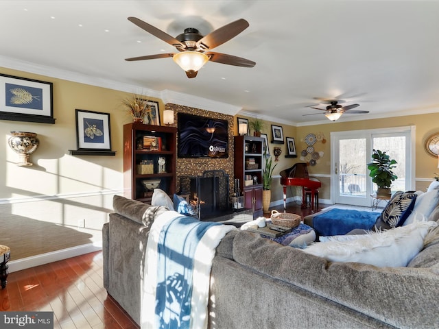 living area featuring baseboards, ornamental molding, a fireplace, wood finished floors, and a ceiling fan