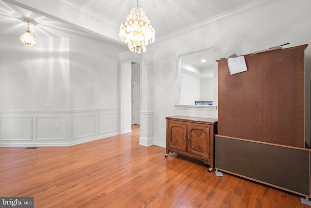 dining space featuring ornamental molding, a chandelier, a wainscoted wall, a decorative wall, and wood finished floors