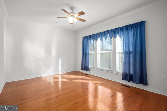 unfurnished room with hardwood / wood-style flooring, a ceiling fan, baseboards, visible vents, and ornamental molding
