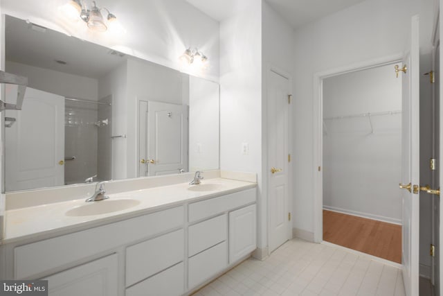 full bath featuring double vanity, baseboards, a sink, and walk in shower