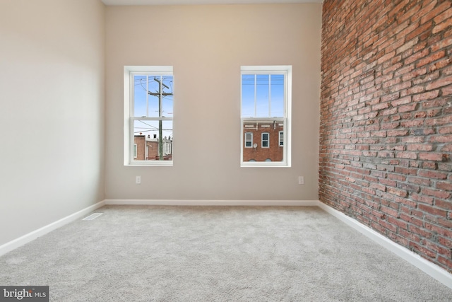 carpeted empty room featuring visible vents, baseboards, and brick wall
