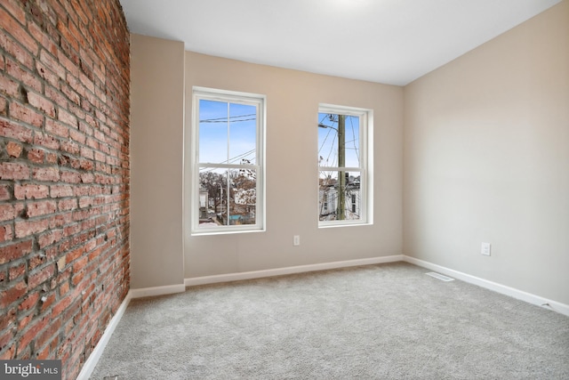 carpeted empty room featuring visible vents, baseboards, and brick wall