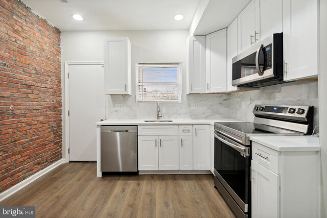 kitchen featuring brick wall, a sink, appliances with stainless steel finishes, light wood-type flooring, and backsplash