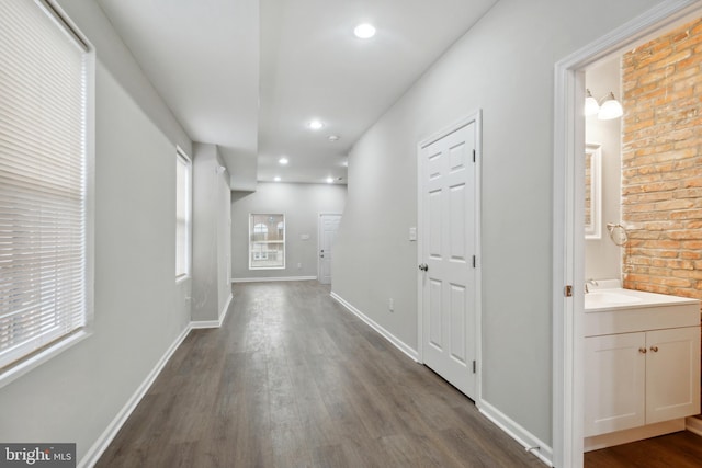 hallway featuring recessed lighting, dark wood-type flooring, baseboards, and a sink