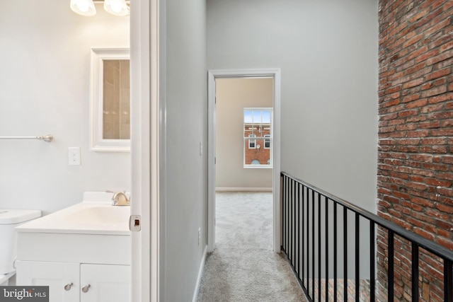 hall with an upstairs landing, carpet, baseboards, and a sink
