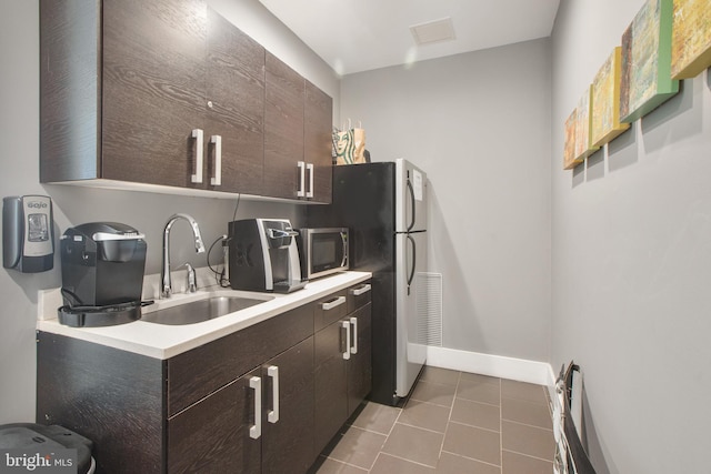 kitchen featuring dark brown cabinetry, light countertops, tile patterned floors, a sink, and appliances with stainless steel finishes