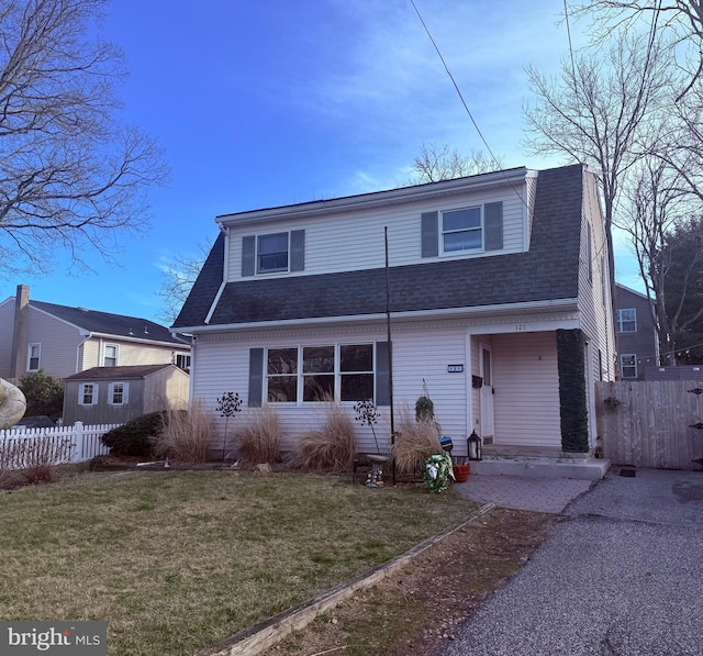 view of front of property featuring a shingled roof, fence, and a front lawn