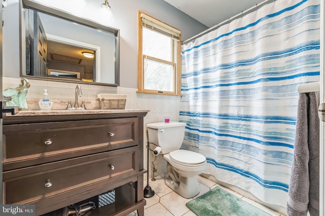 full bath with toilet, vanity, wainscoting, tile patterned flooring, and tile walls