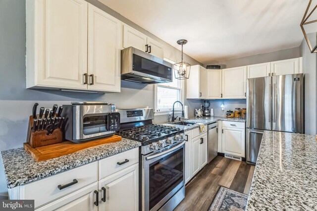 kitchen featuring white cabinetry, dark wood-type flooring, a sink, light stone counters, and appliances with stainless steel finishes
