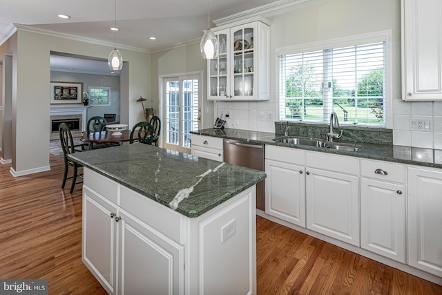 kitchen featuring a sink, crown molding, a kitchen island, light wood-style floors, and glass insert cabinets