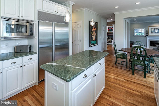 kitchen with built in appliances, ornamental molding, light wood-type flooring, a kitchen island, and white cabinetry