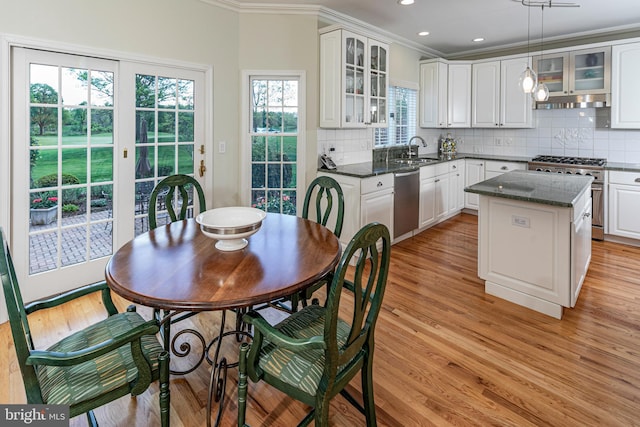 kitchen featuring stainless steel appliances, a sink, crown molding, glass insert cabinets, and backsplash