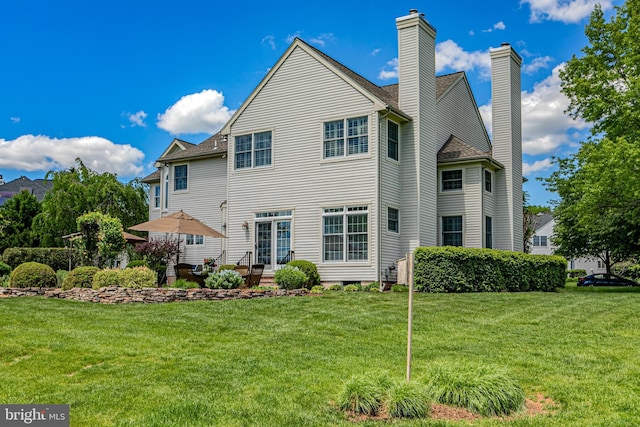 rear view of property with a chimney, a yard, and a patio
