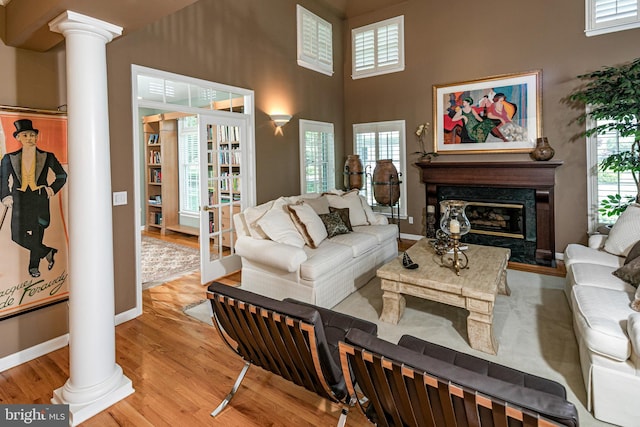 living area with ornate columns, light wood-style floors, a high ceiling, baseboards, and plenty of natural light