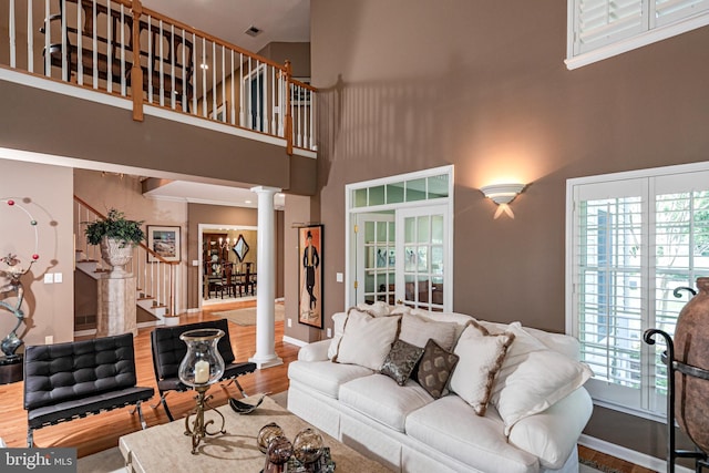 living room with decorative columns, a high ceiling, stairs, and wood finished floors
