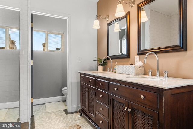 bathroom with double vanity, toilet, baseboards, and a sink