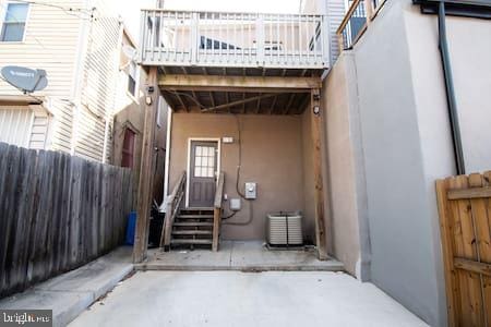 view of exterior entry with a balcony, fence, central AC unit, and stucco siding