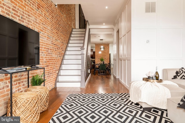 foyer featuring a decorative wall, visible vents, hardwood / wood-style flooring, stairs, and brick wall
