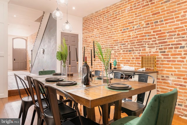 dining area with light wood-style floors, arched walkways, and brick wall