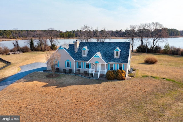 colonial inspired home with a water view, gravel driveway, a chimney, a front lawn, and a shingled roof