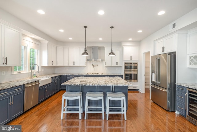 kitchen featuring a sink, visible vents, wall chimney exhaust hood, appliances with stainless steel finishes, and wine cooler