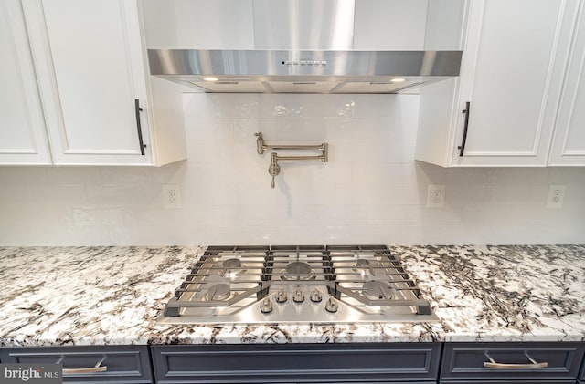 kitchen featuring wall chimney exhaust hood, white cabinets, stainless steel gas cooktop, decorative backsplash, and light stone counters