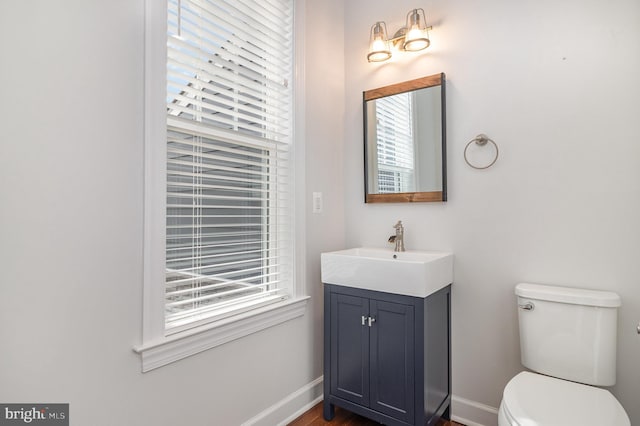 half bath with a healthy amount of sunlight, vanity, and baseboards