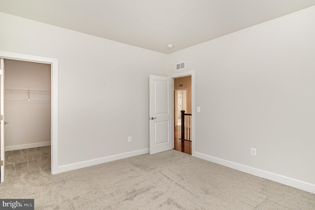 unfurnished bedroom with baseboards, visible vents, a spacious closet, and carpet flooring