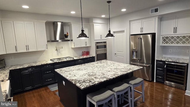 kitchen featuring wall chimney range hood, visible vents, a kitchen island, beverage cooler, and appliances with stainless steel finishes