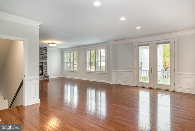 unfurnished living room with a wainscoted wall, a decorative wall, hardwood / wood-style flooring, a stone fireplace, and ornamental molding