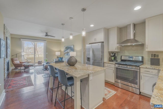 kitchen featuring backsplash, wall chimney exhaust hood, light stone countertops, light wood-style flooring, and stainless steel appliances