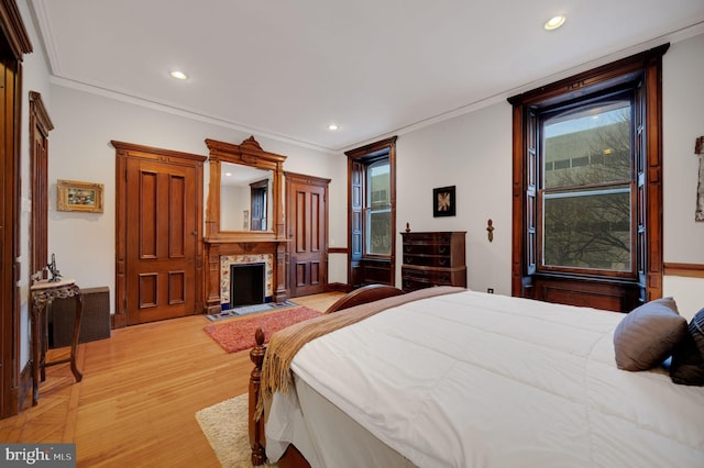 bedroom featuring light wood-type flooring, recessed lighting, ornamental molding, and a premium fireplace