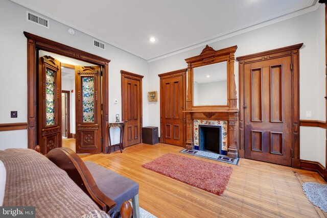 living area featuring a high end fireplace, light wood-type flooring, ornamental molding, and visible vents