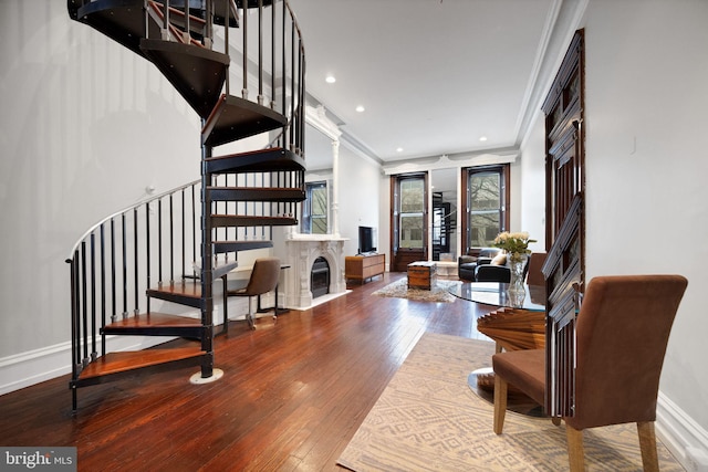 living area featuring a glass covered fireplace, stairway, crown molding, and hardwood / wood-style flooring