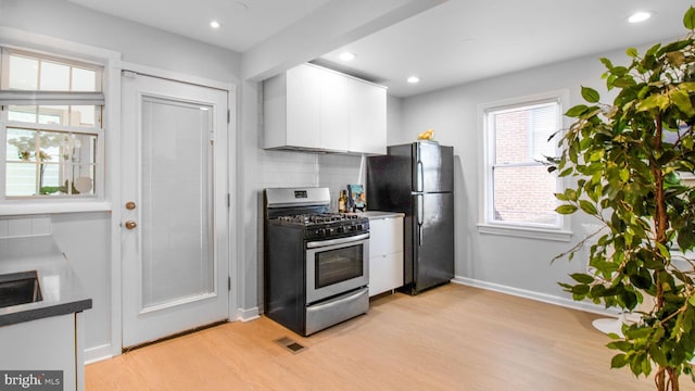 kitchen featuring freestanding refrigerator, white cabinets, stainless steel gas range oven, and light wood-style flooring