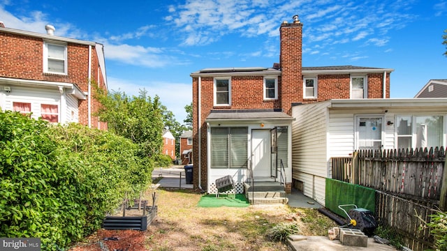 rear view of property with fence, brick siding, a vegetable garden, entry steps, and a chimney