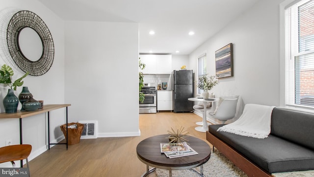 living area with visible vents, light wood finished floors, baseboards, and a healthy amount of sunlight