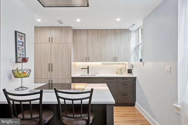 kitchen with light brown cabinetry, modern cabinets, a sink, light wood finished floors, and recessed lighting