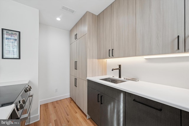 kitchen with a sink, stainless steel range with electric cooktop, baseboards, light wood-style flooring, and light countertops