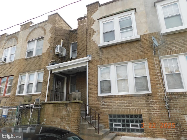 townhome / multi-family property with a wall unit AC, fence, and brick siding