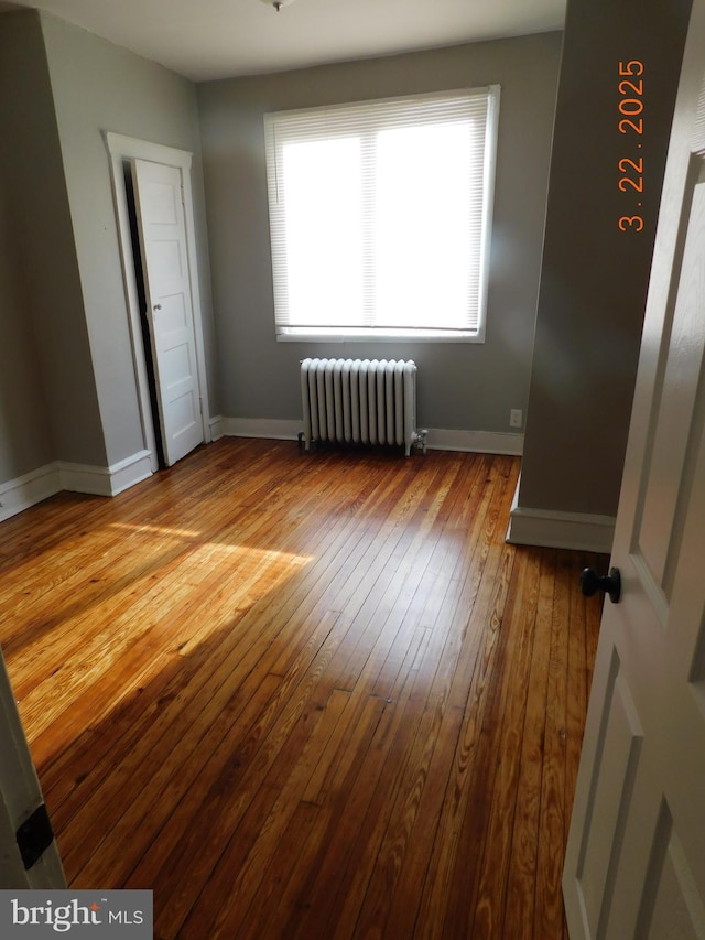 unfurnished bedroom featuring hardwood / wood-style floors, radiator heating unit, and baseboards